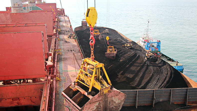 Loading coal from cargo barges onto a bulk carrier using ship cranes and grabs at the port of Samarinda, Indonesia. Close-up view of the work of bulldozers and loaders.
