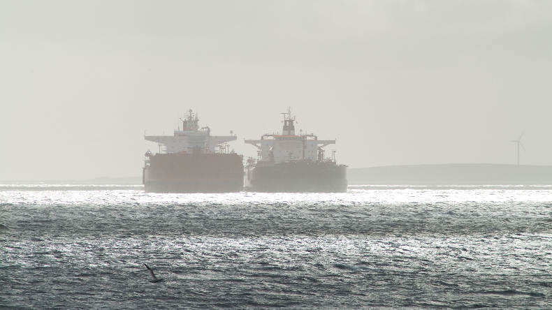 Two oil tankers side by side at sea in the distance on a sunlit sea