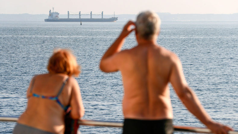 A couple in Odesa watch one of the grain ships leaving the port